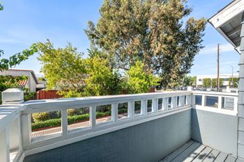 A balcony with a white railing and a view of trees and buildings.